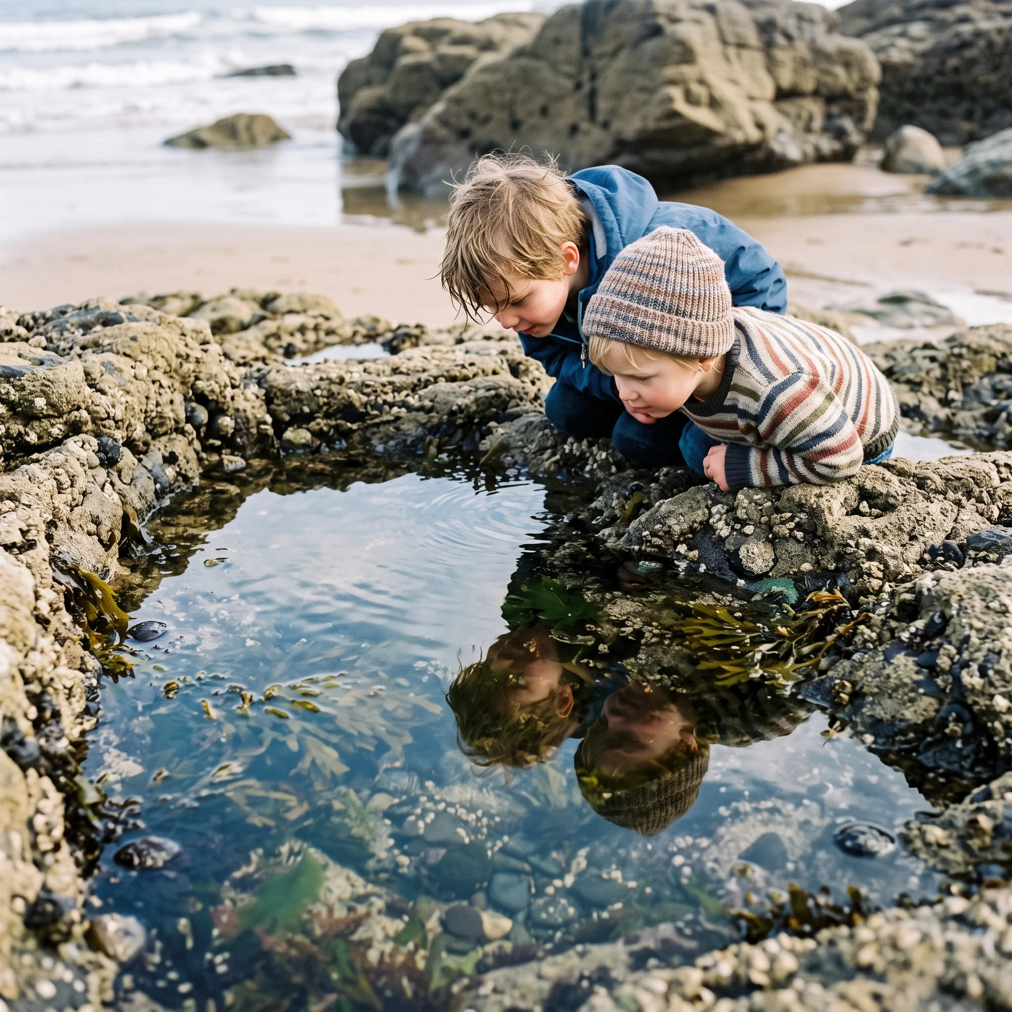 Two children lean over a rock pool, their faces reflected in the water.