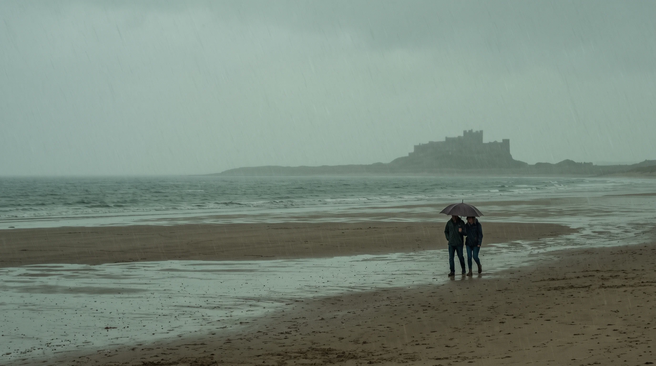 Two small figures share an umbrella far out on a rain-soaked beach, a castle grey on the headland behind