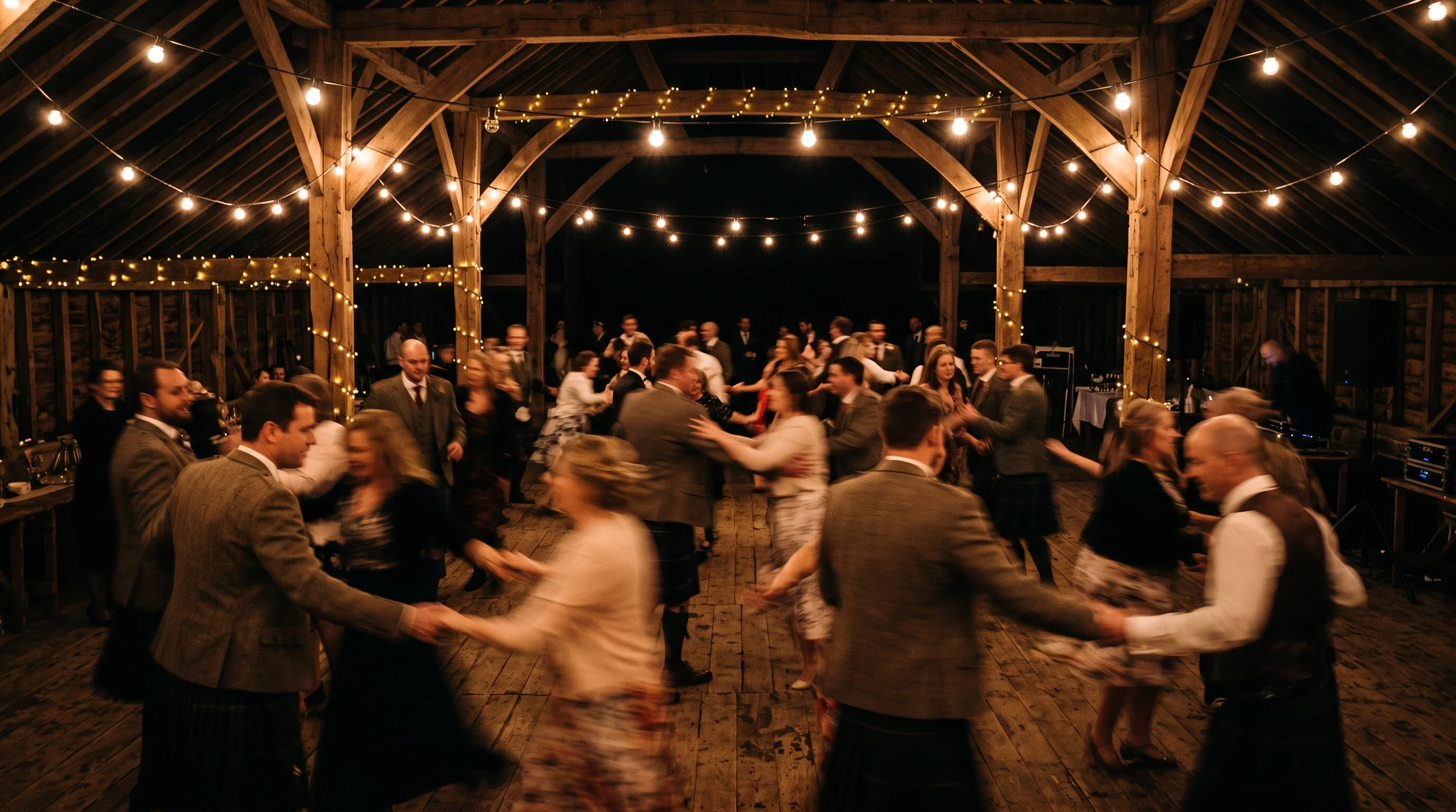 Dancers blur into streaks under festoon bulbs during a ceilidh in a dark barn
