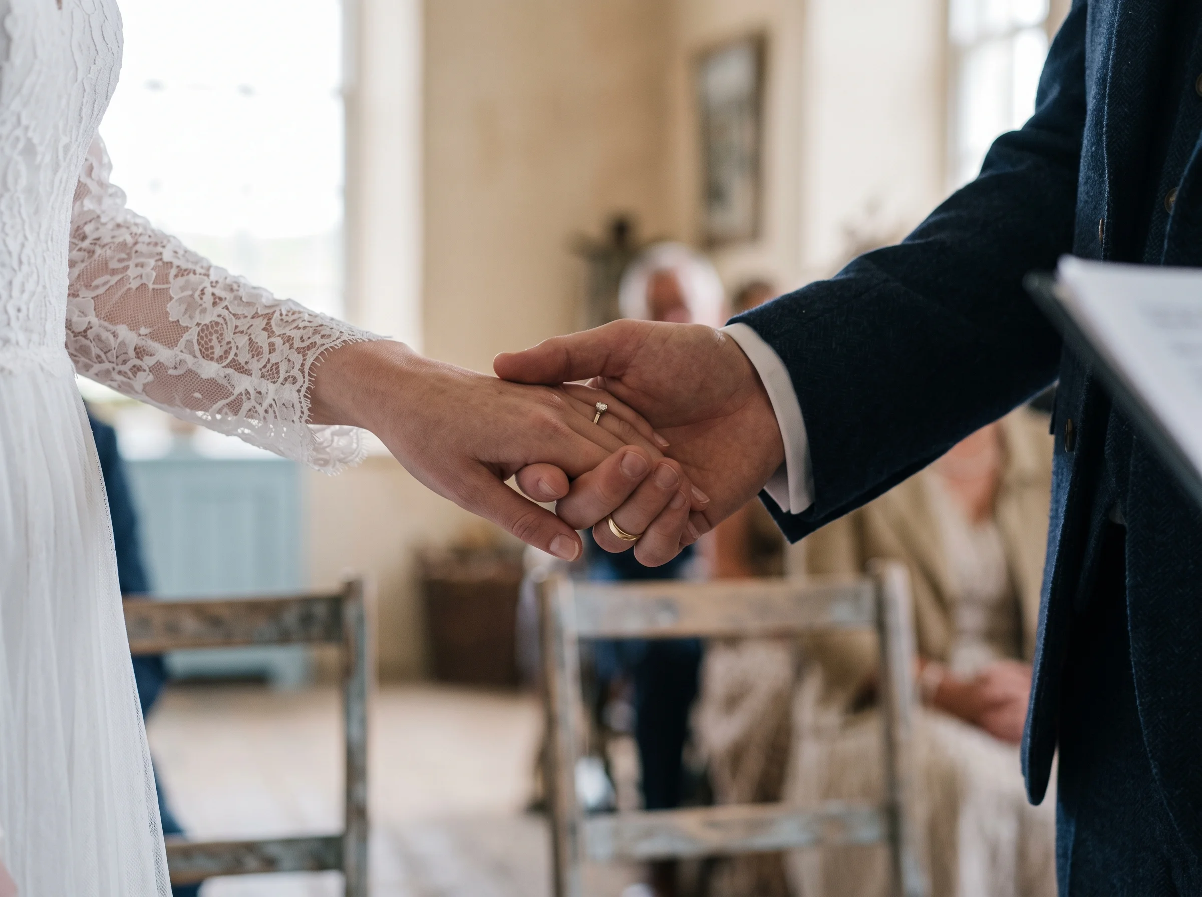 Two hands held tightly during the vows, a suit sleeve and a lace cuff