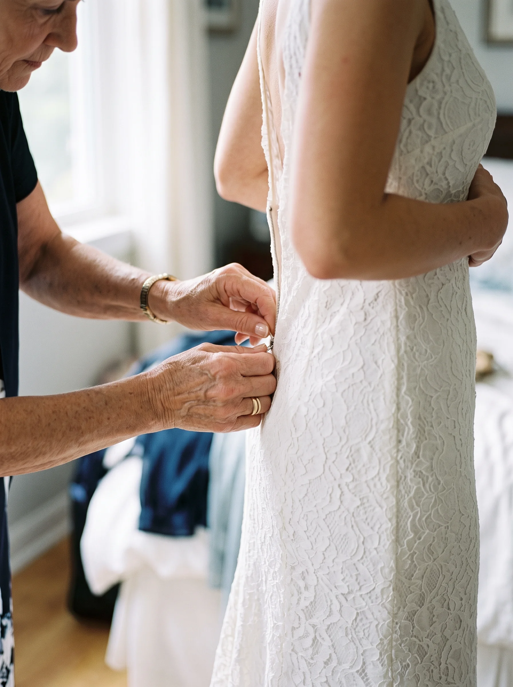 A mother's hands fasten the zip at the back of a wedding dress