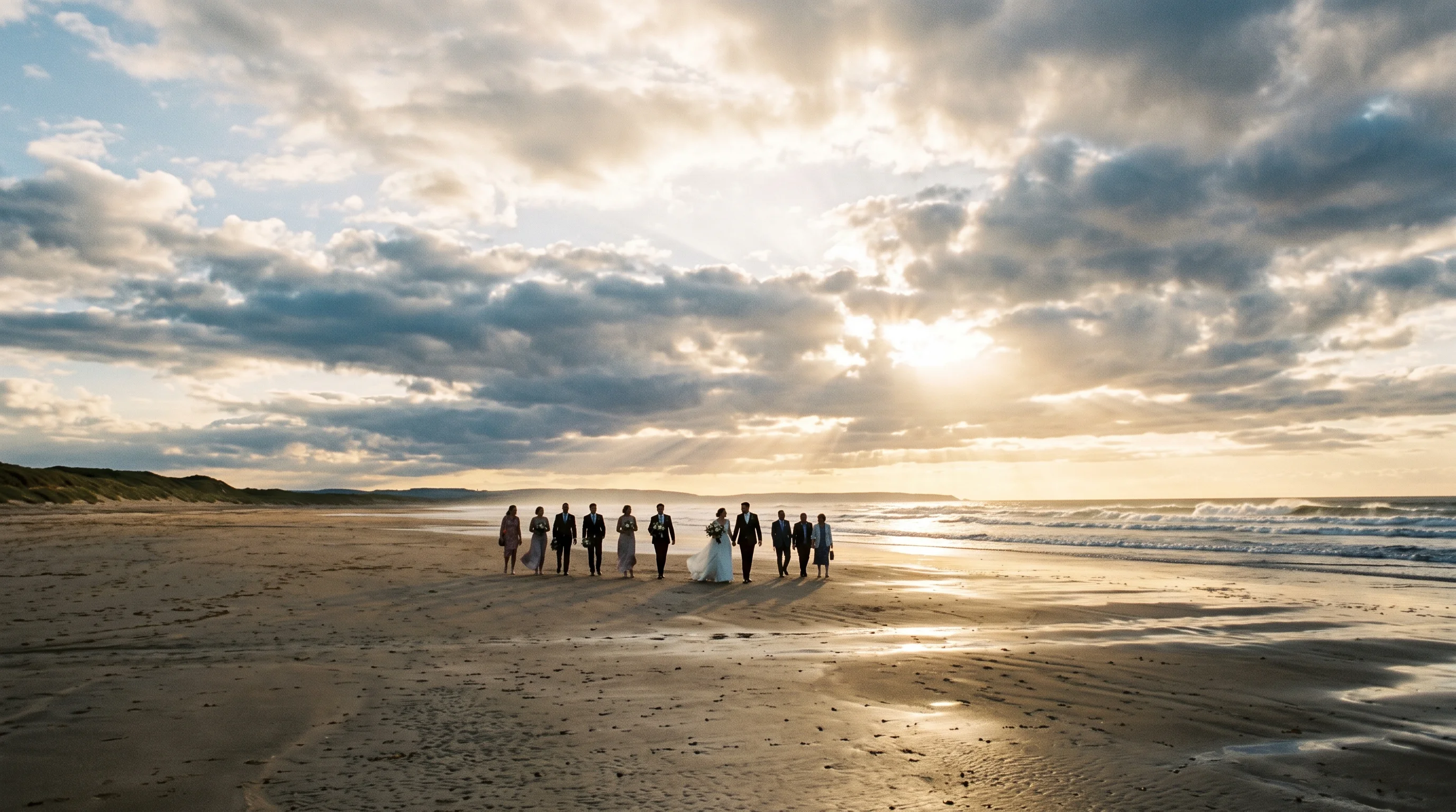The wedding party walk back across a vast empty beach towards the dunes under a huge late-afternoon sky