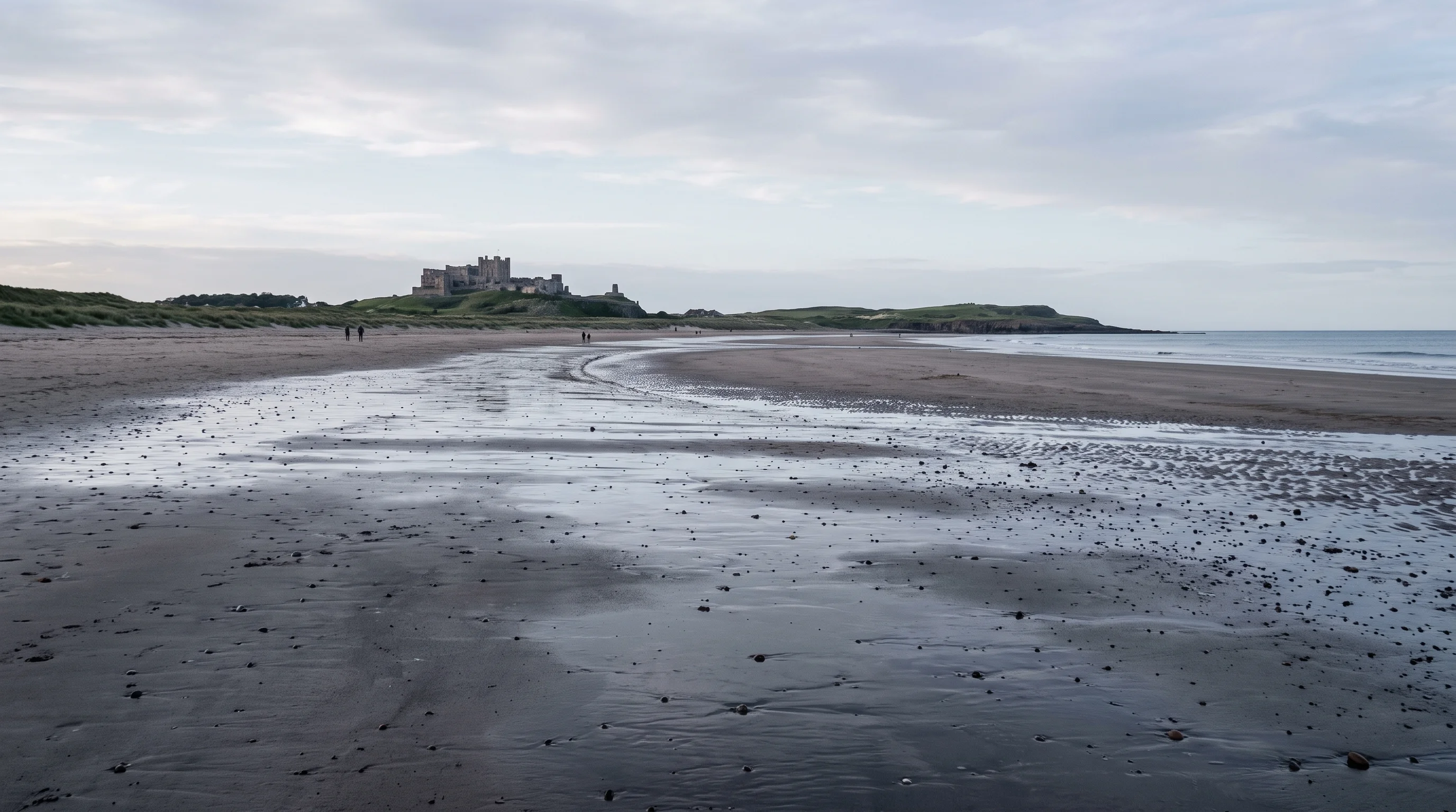A near-empty beach at low tide with wet sand reflecting the sky and a castle far off on the headland